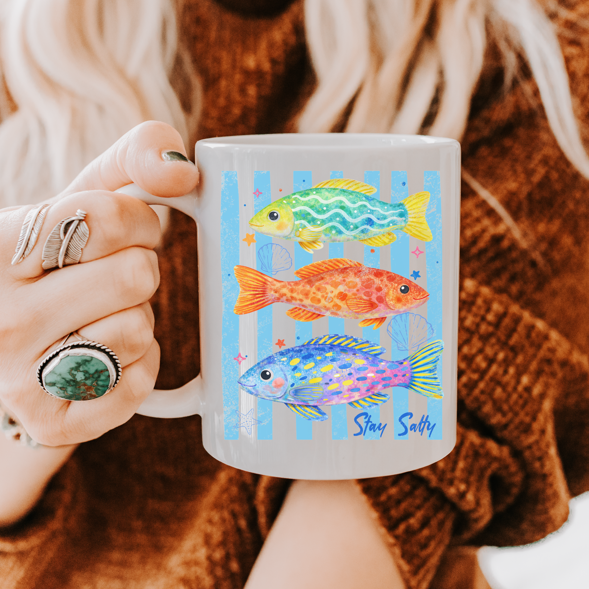 Person holding a mug with colorful fish design and 'Stay Salty' text.