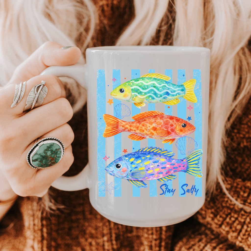 Mug with fish design and 'Stay Salty' text held by a person wearing rings.