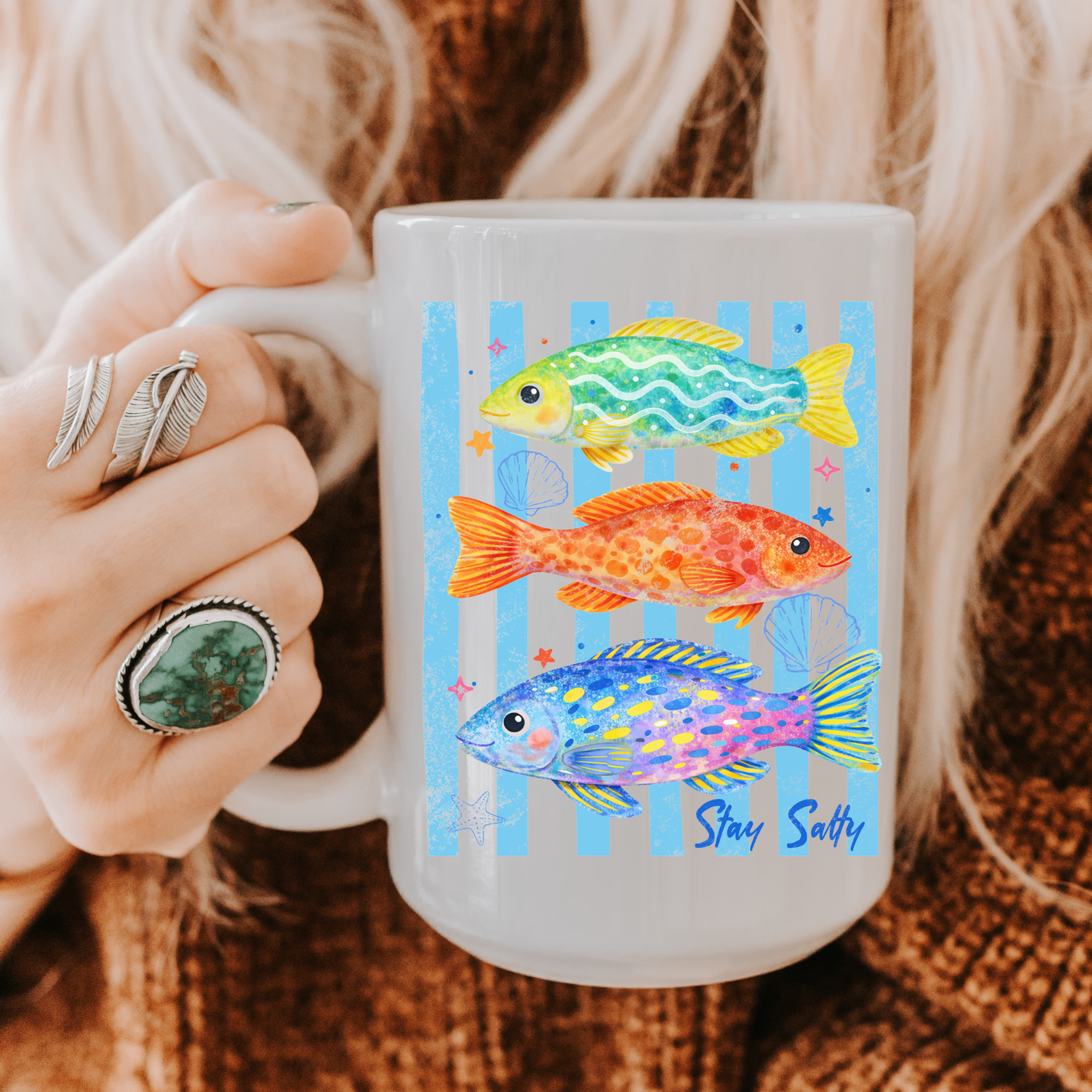 Mug with fish design and 'Stay Salty' text held by a person wearing rings.