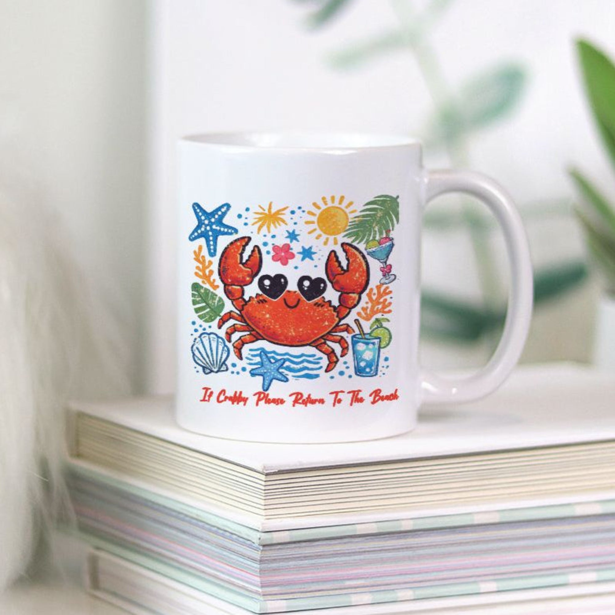 White mug with a colorful crab design on a stack of books with plants in the background