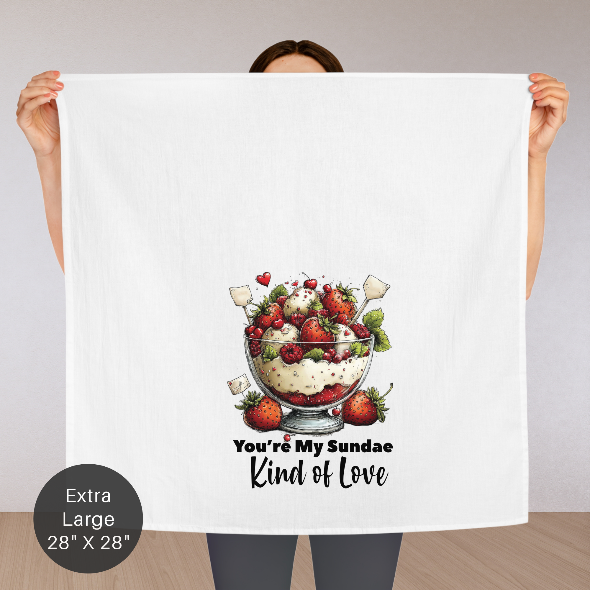 Person holding an extra large tea towel with a dessert illustration and text ' You're My Sundae Kind of Love'.