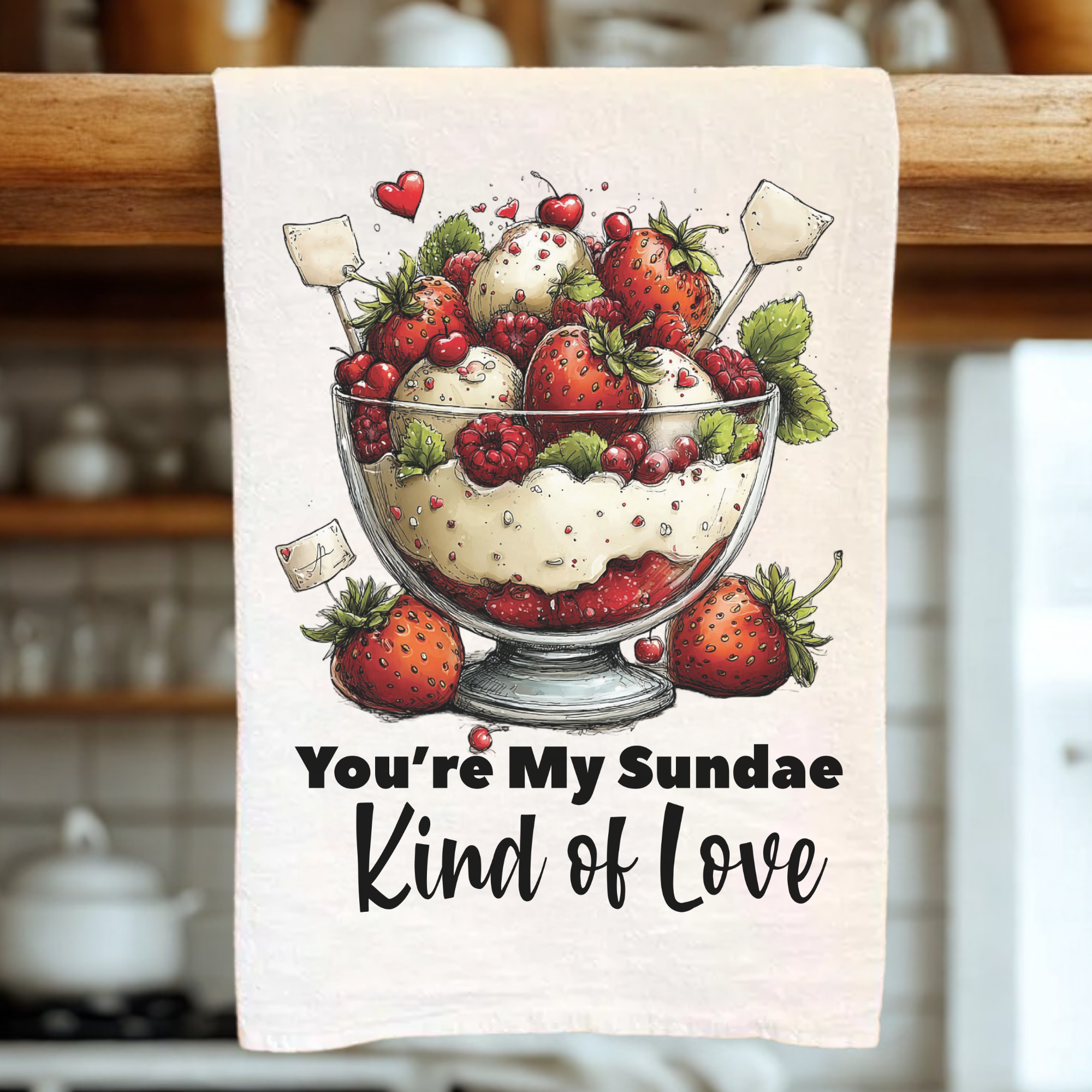Tea towel with a dessert illustration and text 'You're My Sundae Kind of Love' in a kitchen setting.