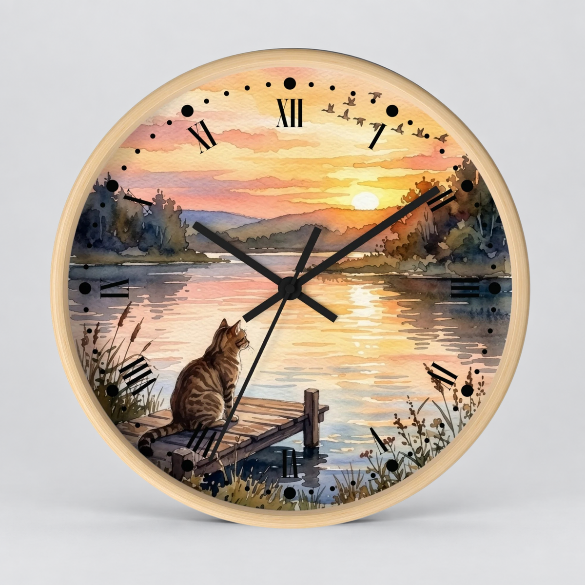 Round wall clock with a light wood frame and a scenic watercolor print of a cat sitting on a dock by a lake at sunset, with black Roman numerals and clock hands on a light gray background.