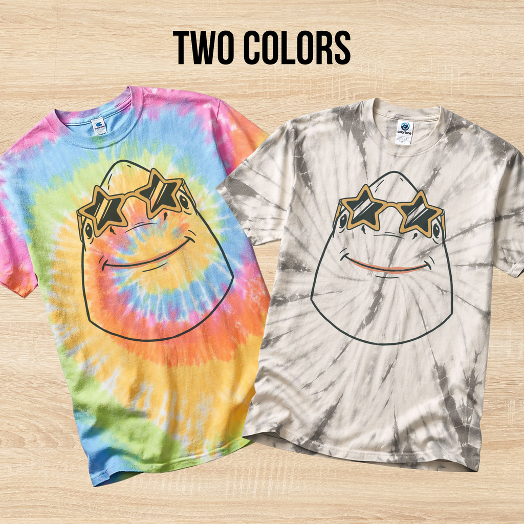 Two tie-dye t-shirts in the colors Eternity and Spider Silver with a graphic design of a shark wearing star shaped sunglasses on a wooden surface