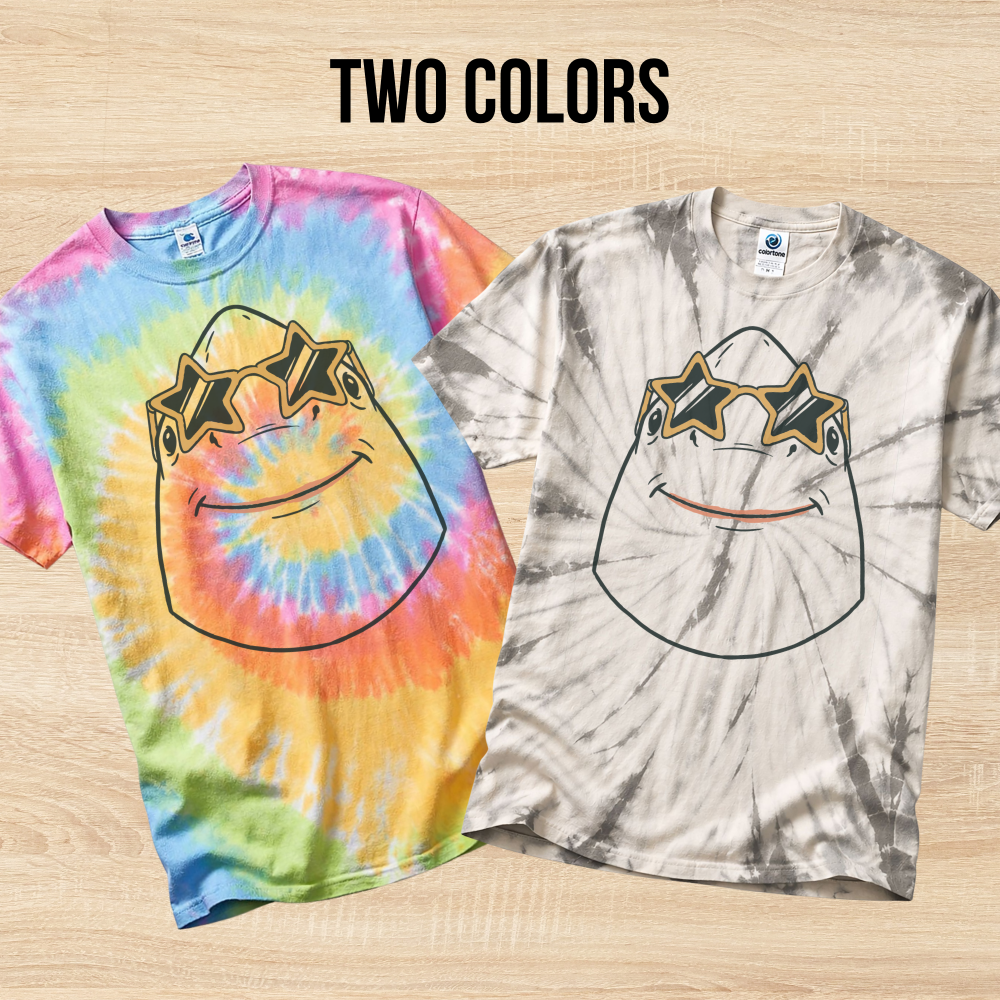 Two tie-dye t-shirts in the colors Eternity and Spider Silver with a graphic design of a shark wearing star shaped sunglasses on a wooden surface