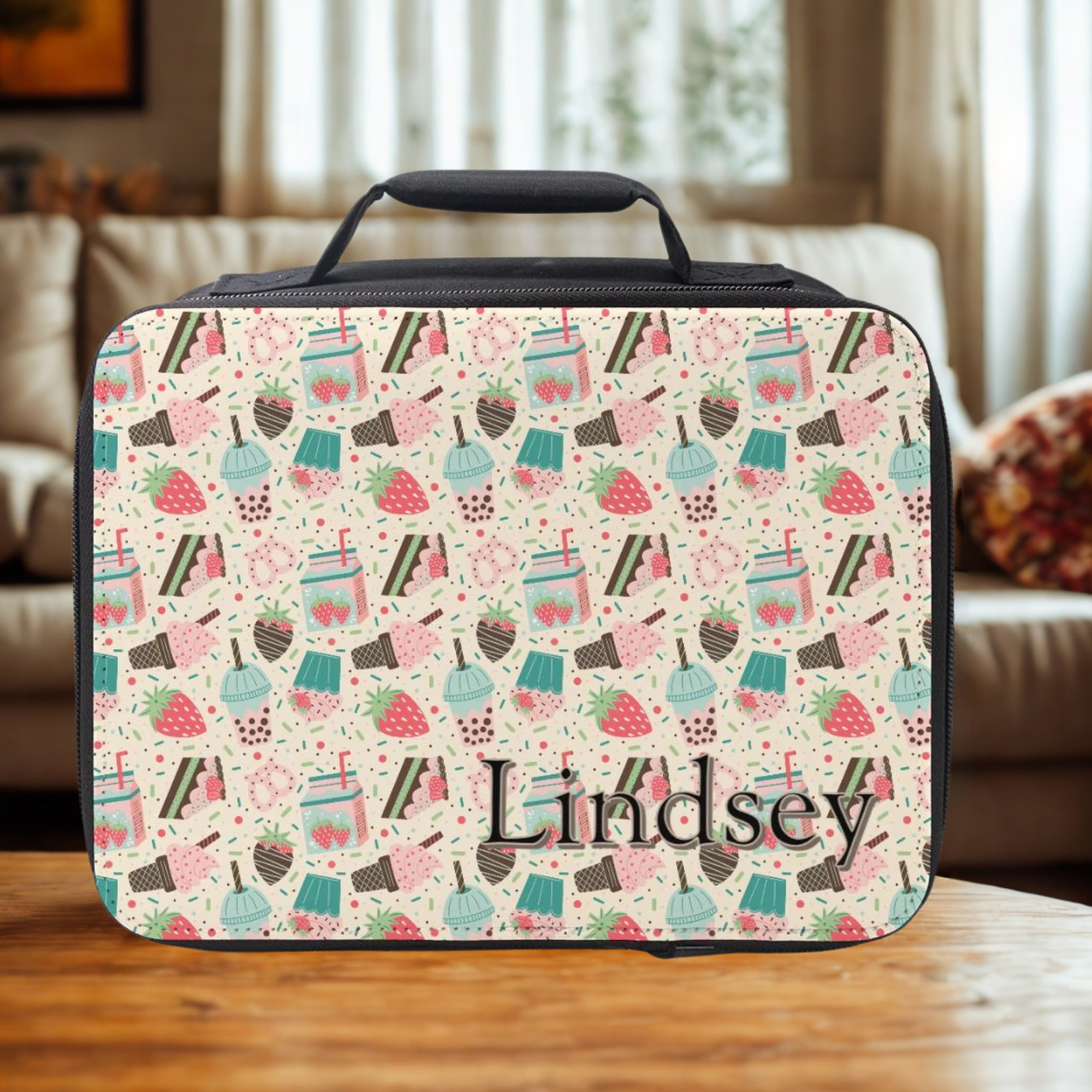 Black insulated lunch bag with a strawberry desert pattern and personalized with a name on a wooden living room table.