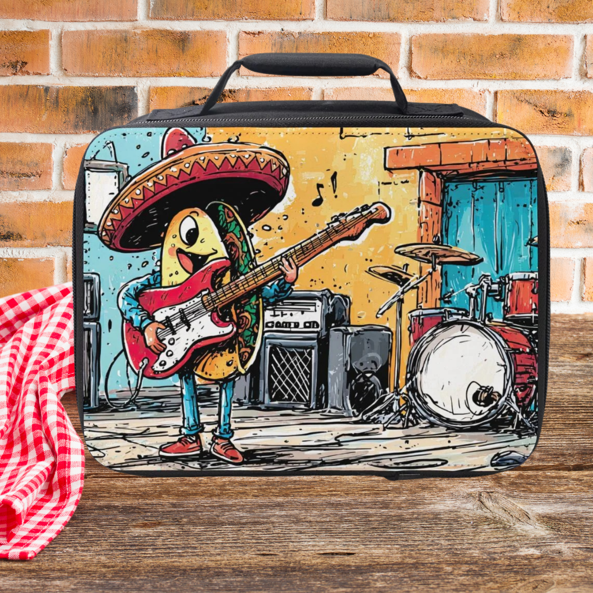 Lunch box with a cartoon character  taco playing guitar and drums on a picnic table against a brick wall background