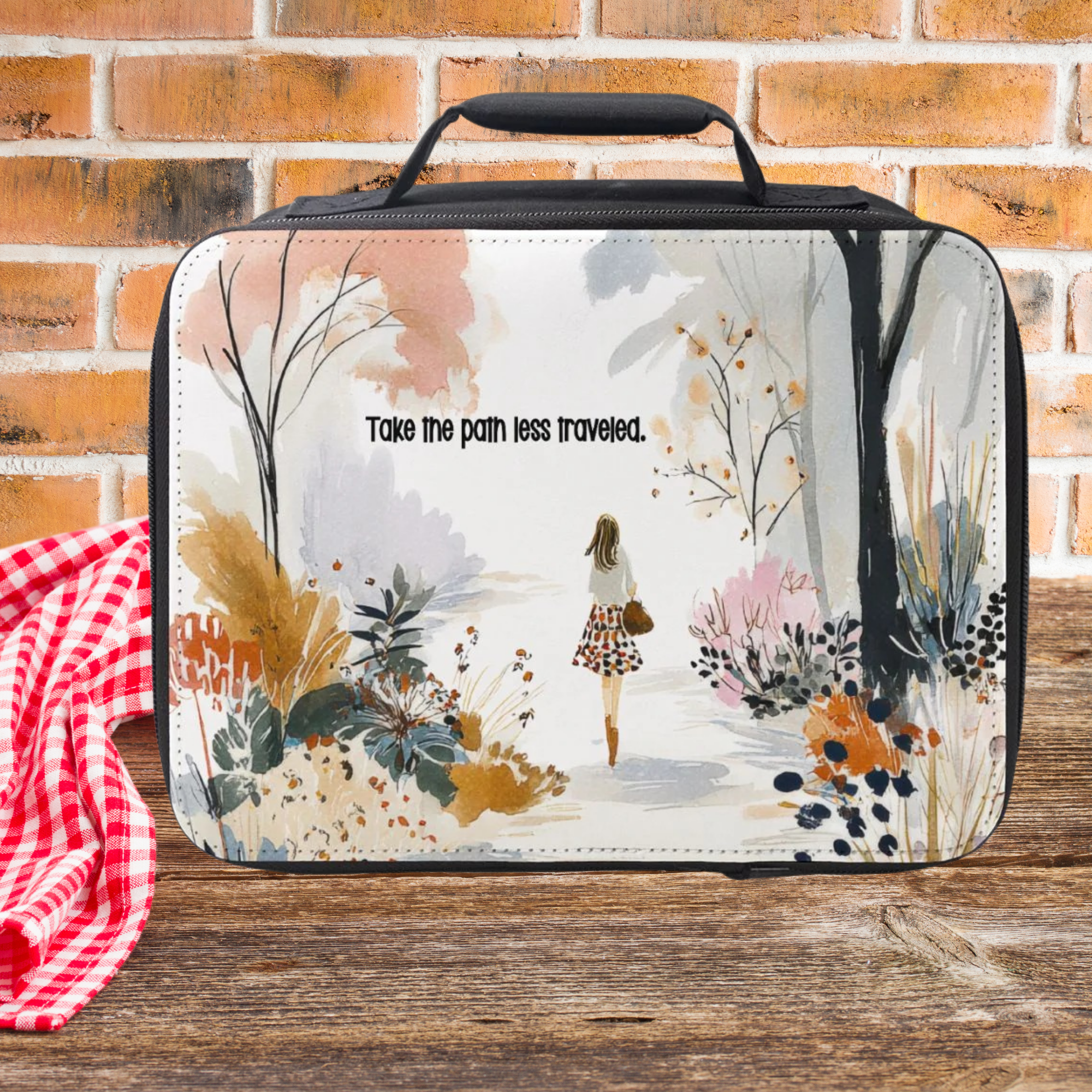  insulated lunch bag with nature-themed design and text 'Take the path less traveled.' on a wooden picnic table with a brick wall background.