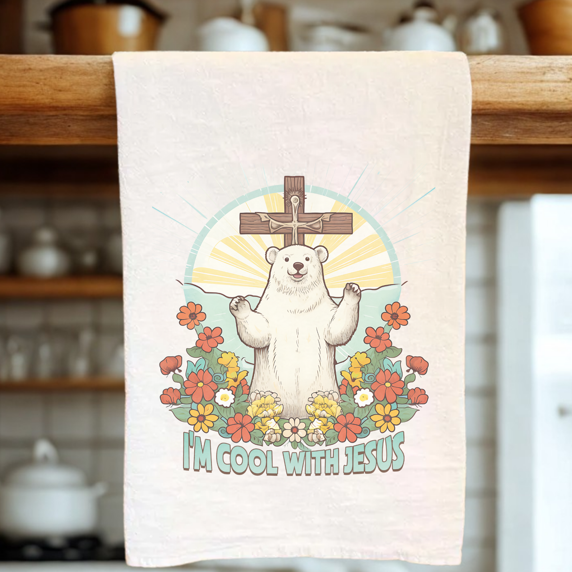 Tea towel with a bear in front of  a cross and flowers, text 'I'm cool with Jesus', on a wooden rack.