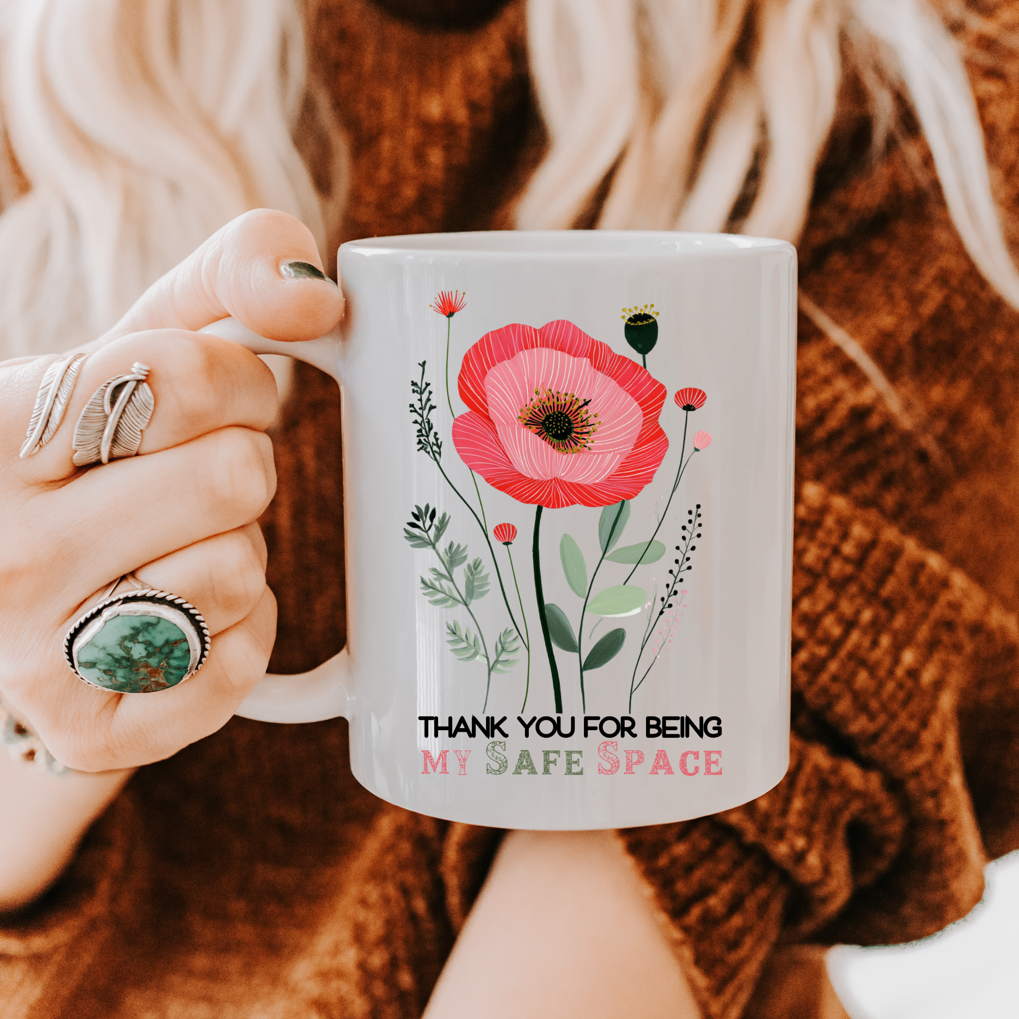 Person holding an 11oz mug with floral design and text 'Thank You For Being My Safe Space', wearing a brown sweater.
