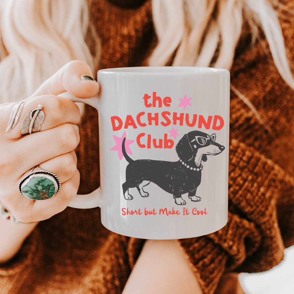 Person holding an 11oz mug with 'the DACHSHUND Club' design, featuring a dachshund dog illustration.