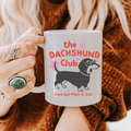 Person holding an 11oz mug with 'the DACHSHUND Club' design, featuring a dachshund dog illustration.