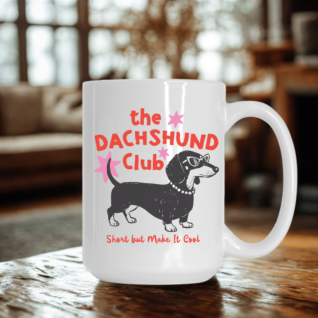 White mug with 'the DACHSHUND Club' design featuring a dachshund dog on a wooden living room table.