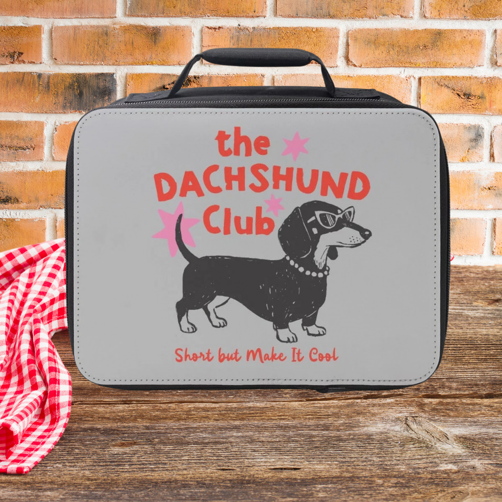 Lunch bag with 'the DACHSHUND Club' text and dachshund illustration on a wooden picnic table with brick background