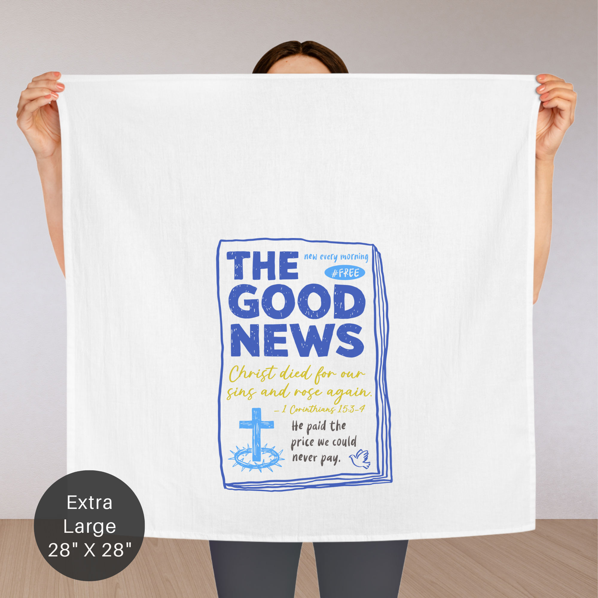 Person holding an extra large white tea towel with 'The Good News' text and cross graphic.