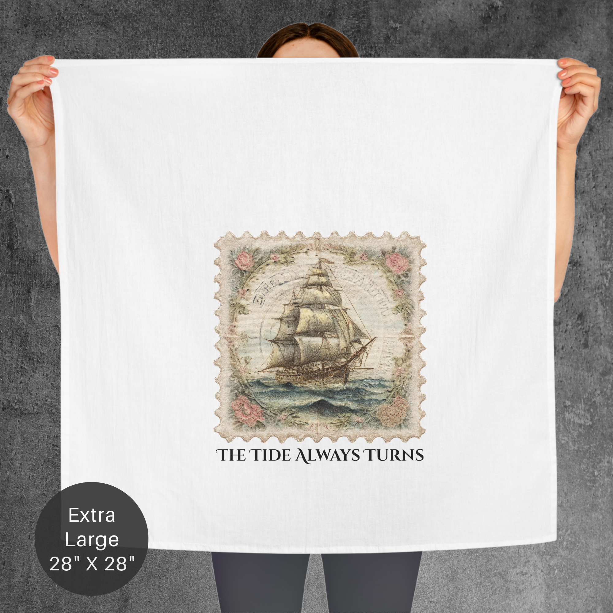 Person holding a large tea towel with a ship design and text 'The Tide Always Turns' on a gray background