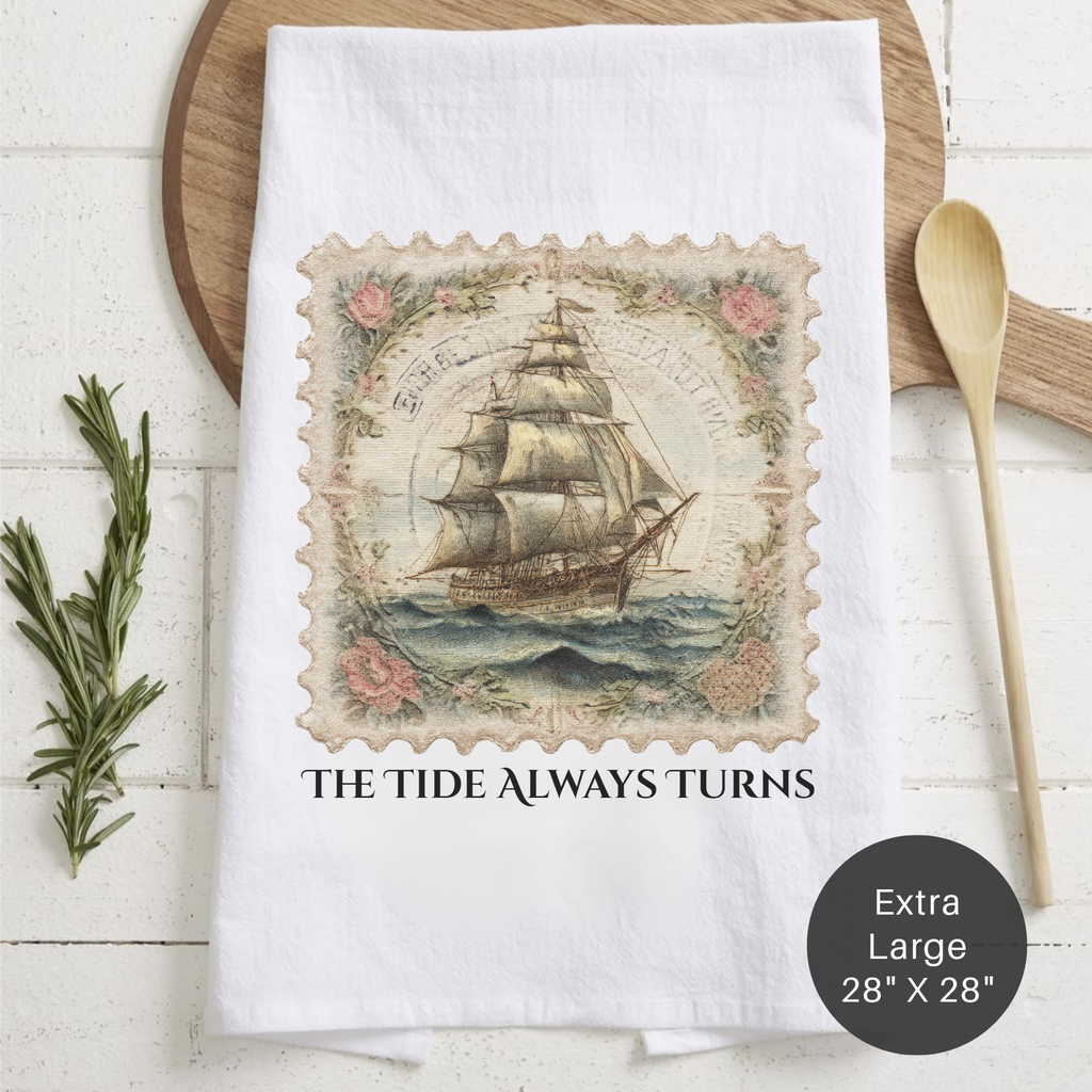 White tea towel with vintage ship design and text 'The Tide Always Turns' on a wooden surface