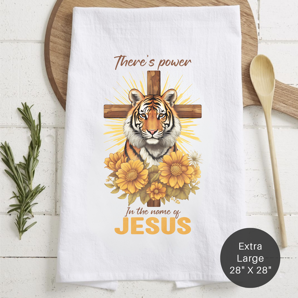White tea towel with a tiger and cross design, text 'There's power in the name of Jesus', on a wooden surface.