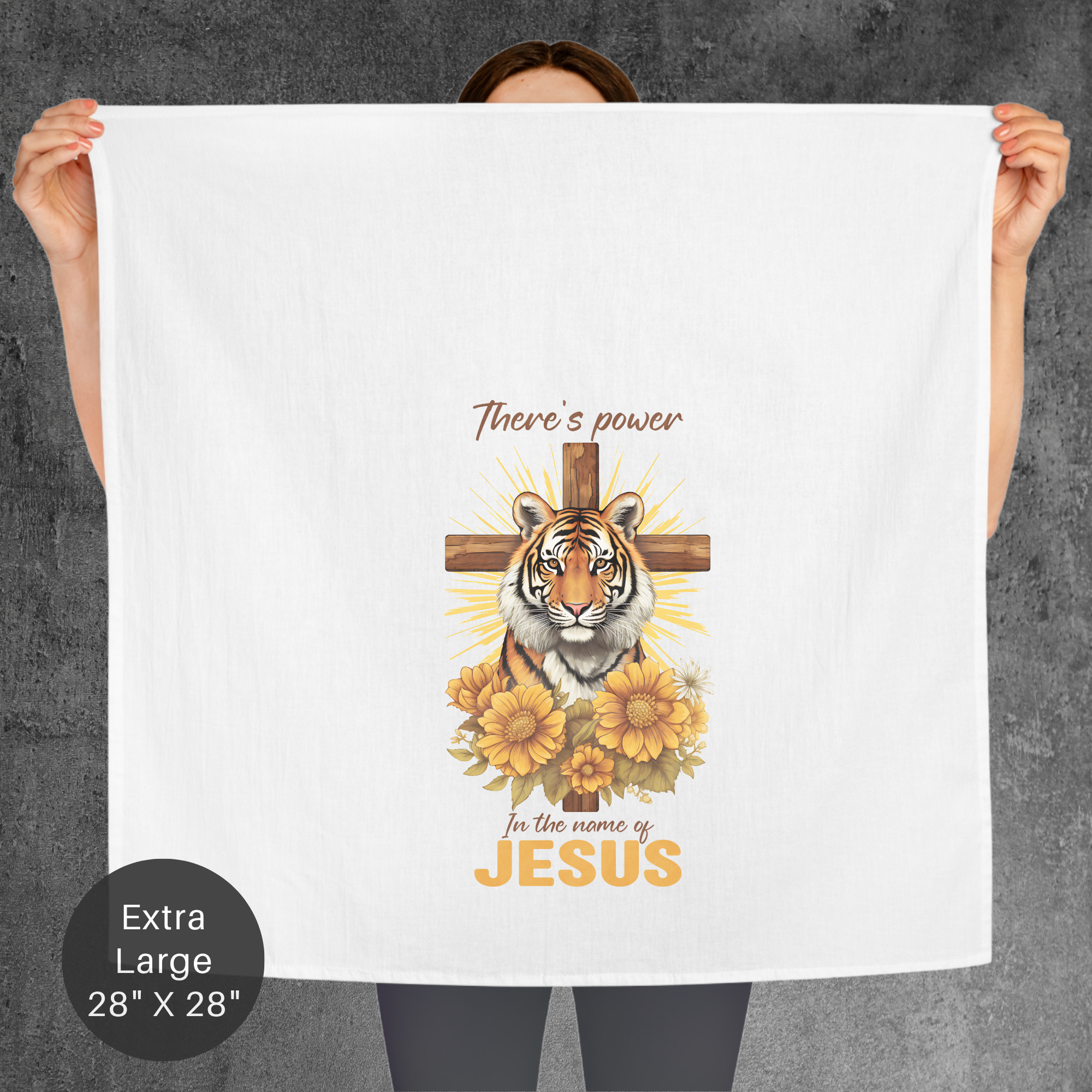 Person holding an extra large tea towel with a tiger, cross, and floral design with text on a gray background