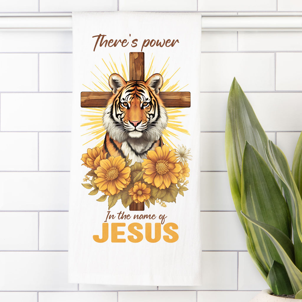 Decorative tea towel with a tiger, cross, and flowers on a white tiled wall.