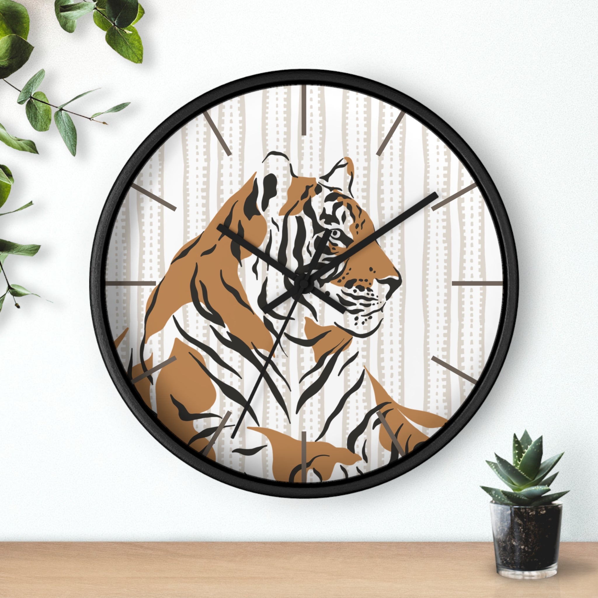 Wall clock with a tiger design on a white wall with a plant and small pot.