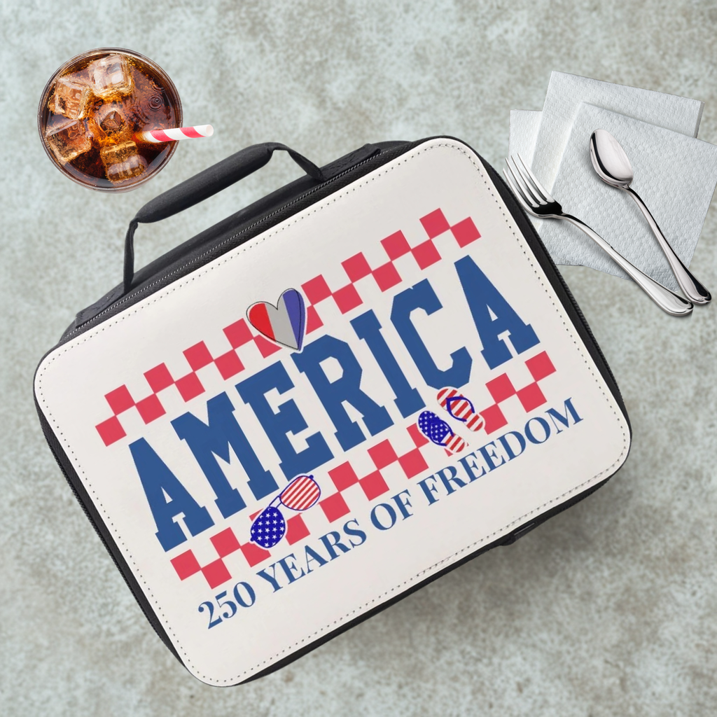 Lunch box with 'America 250 Years of Freedom' design on a gray table with a drink and utensils.