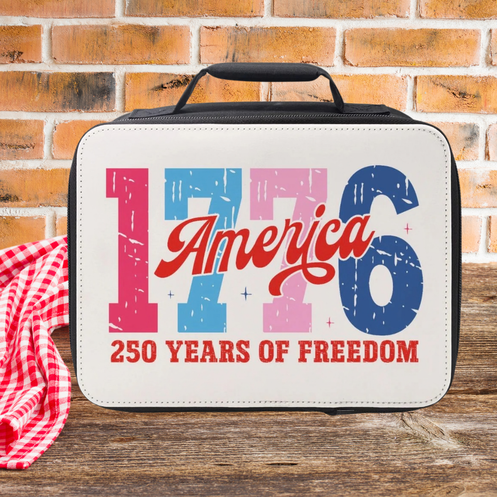 Insulated lunch bag with 'America 1776 250 Years of Freedom' text on a wooden picnic table against a brick wall background