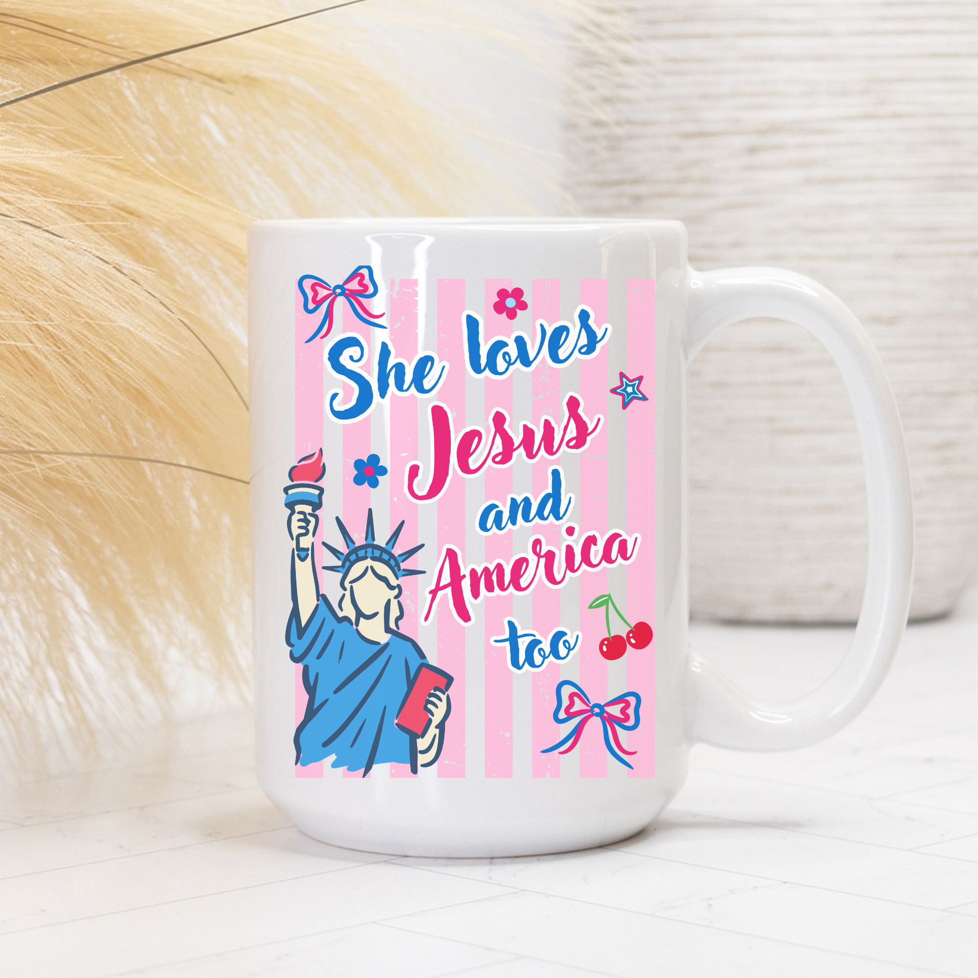 White 15oz. mug with colorful design featuring the Statue of Liberty, text 'She loves Jesus and America too', and decorative elements on a light background.