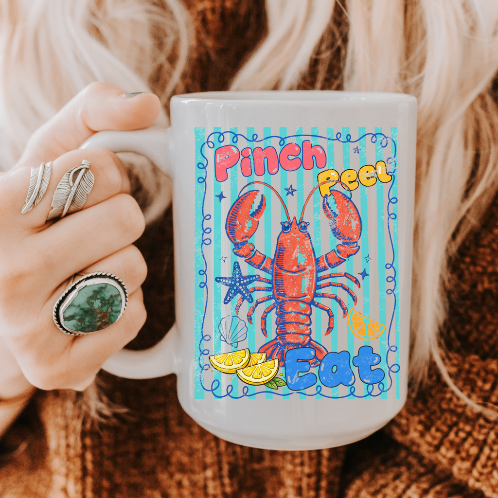 15oz. Mug with a colorful lobster design and text held by a person wearing rings.