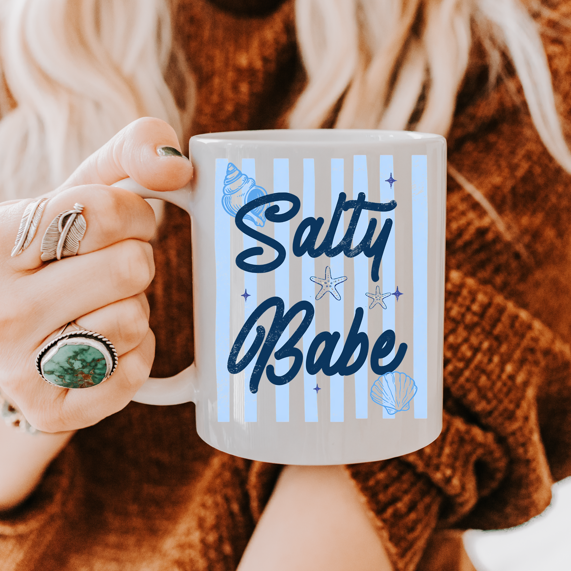 Person holding an 11oz. mug with 'Salty Babe' text and sea-themed design.