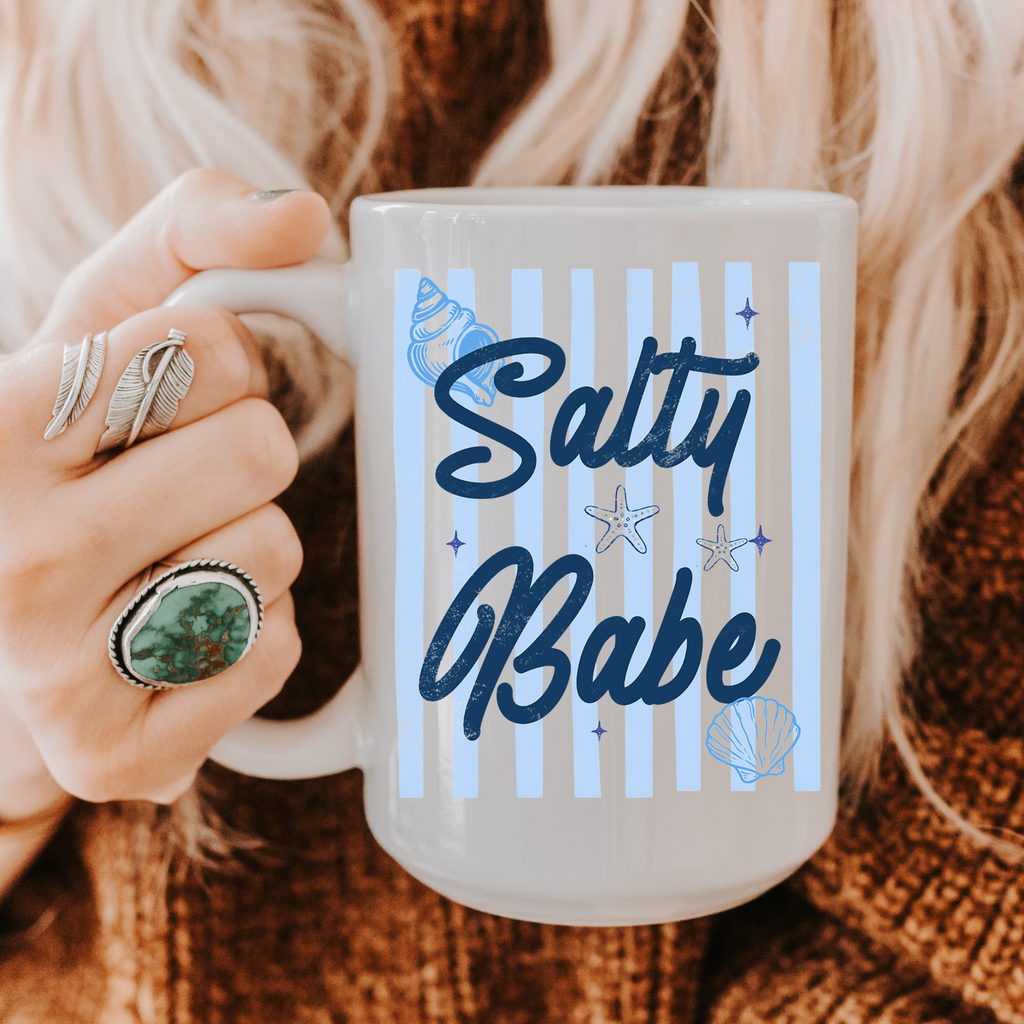 Person holding a 15oz. mug with 'Salty Babe' design on a textured fabric background