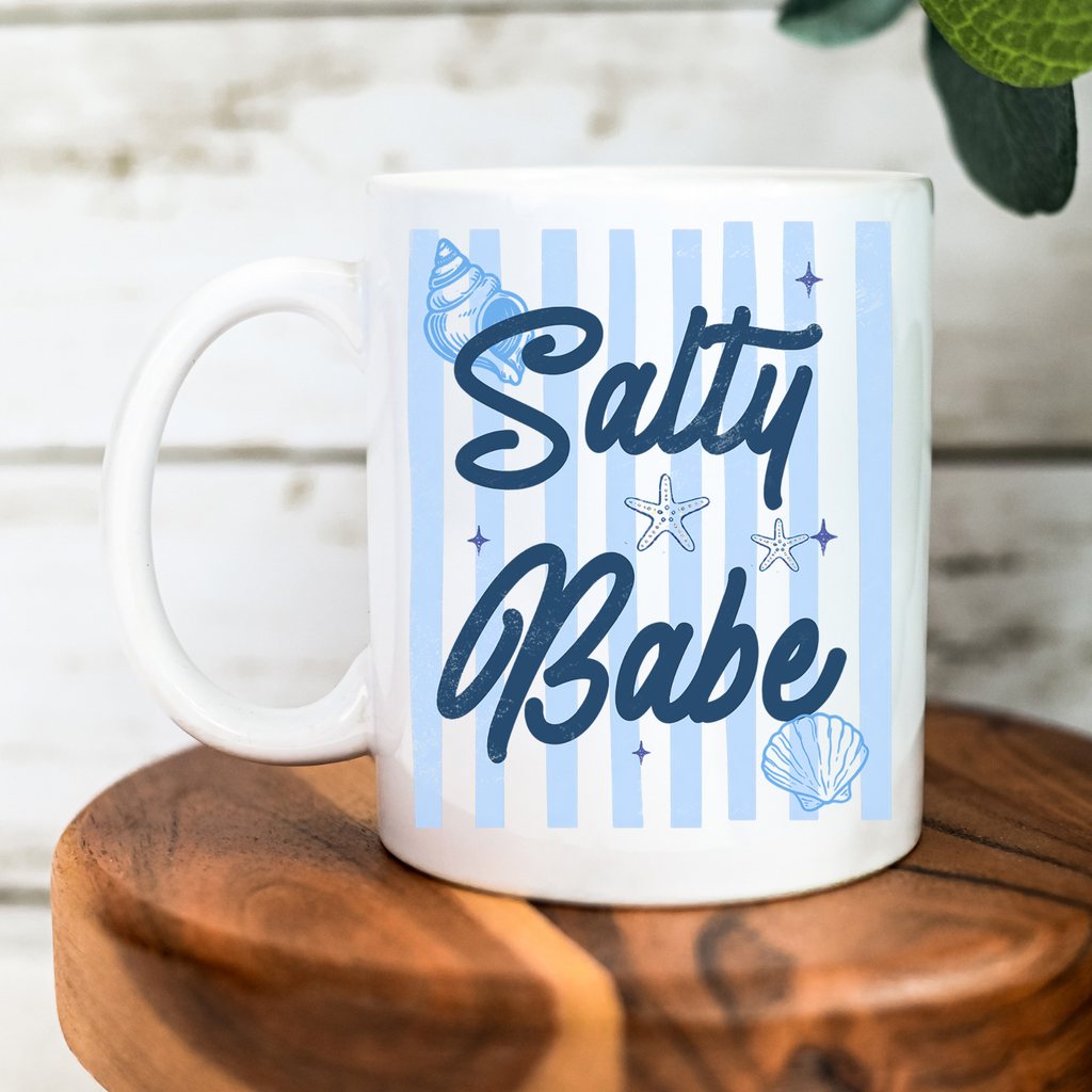 White 11oz. mug with 'Salty Babe' text and nautical designs on a wooden surface.