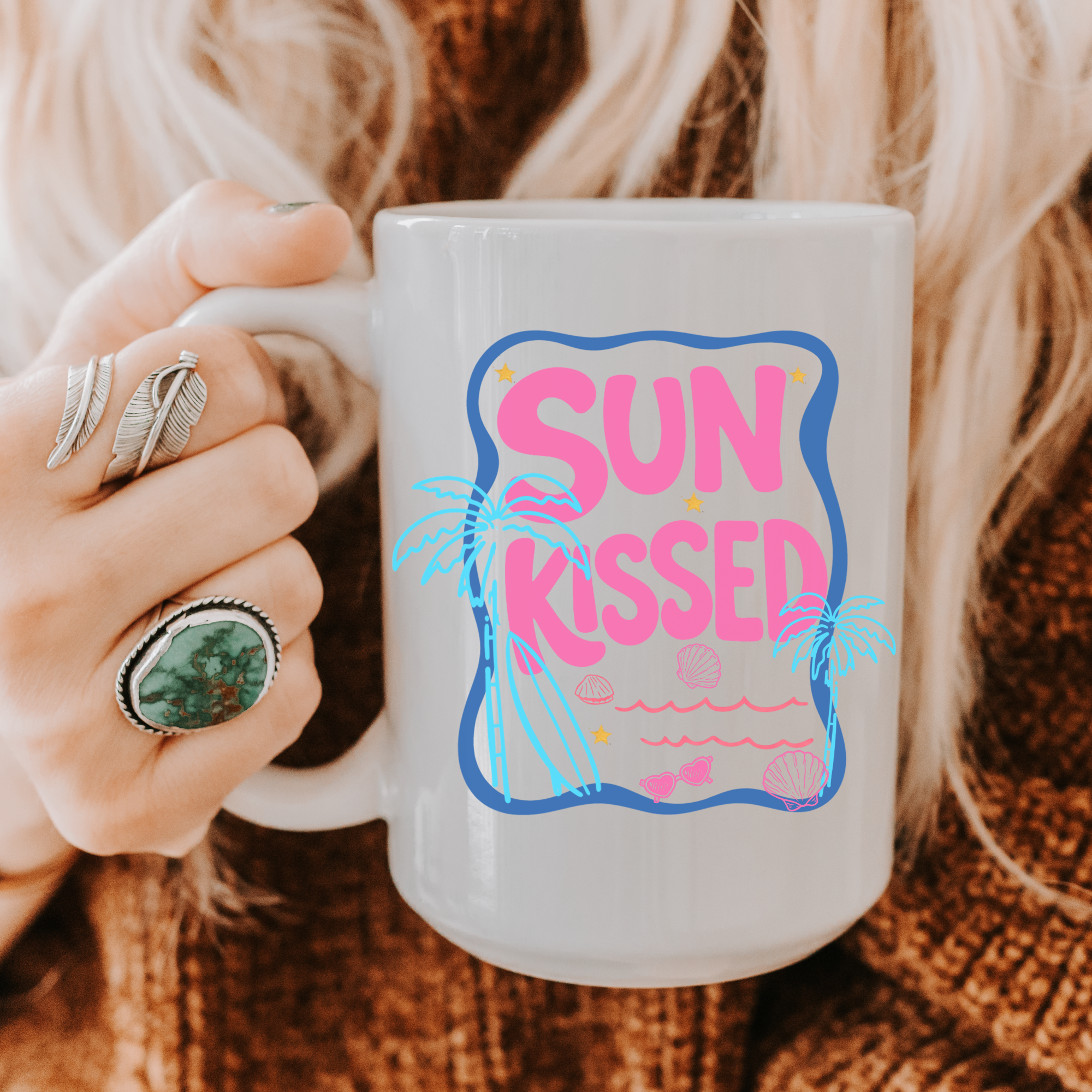 Person holding an 11oz. mug with 'Sun Kissed' design on a textured surface