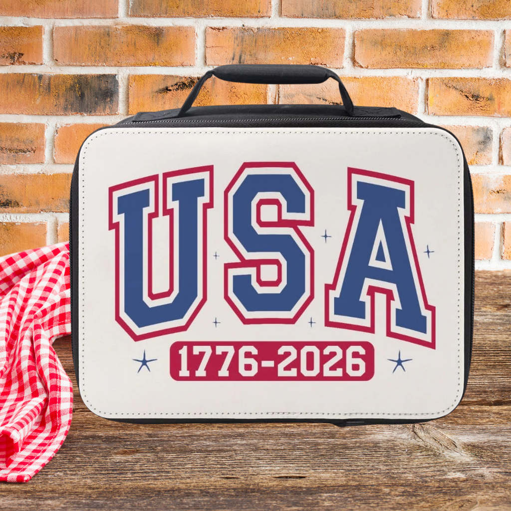 Insulated lunch bag with 'USA 1776-2026' text on a wooden picnic table with a brick wall background