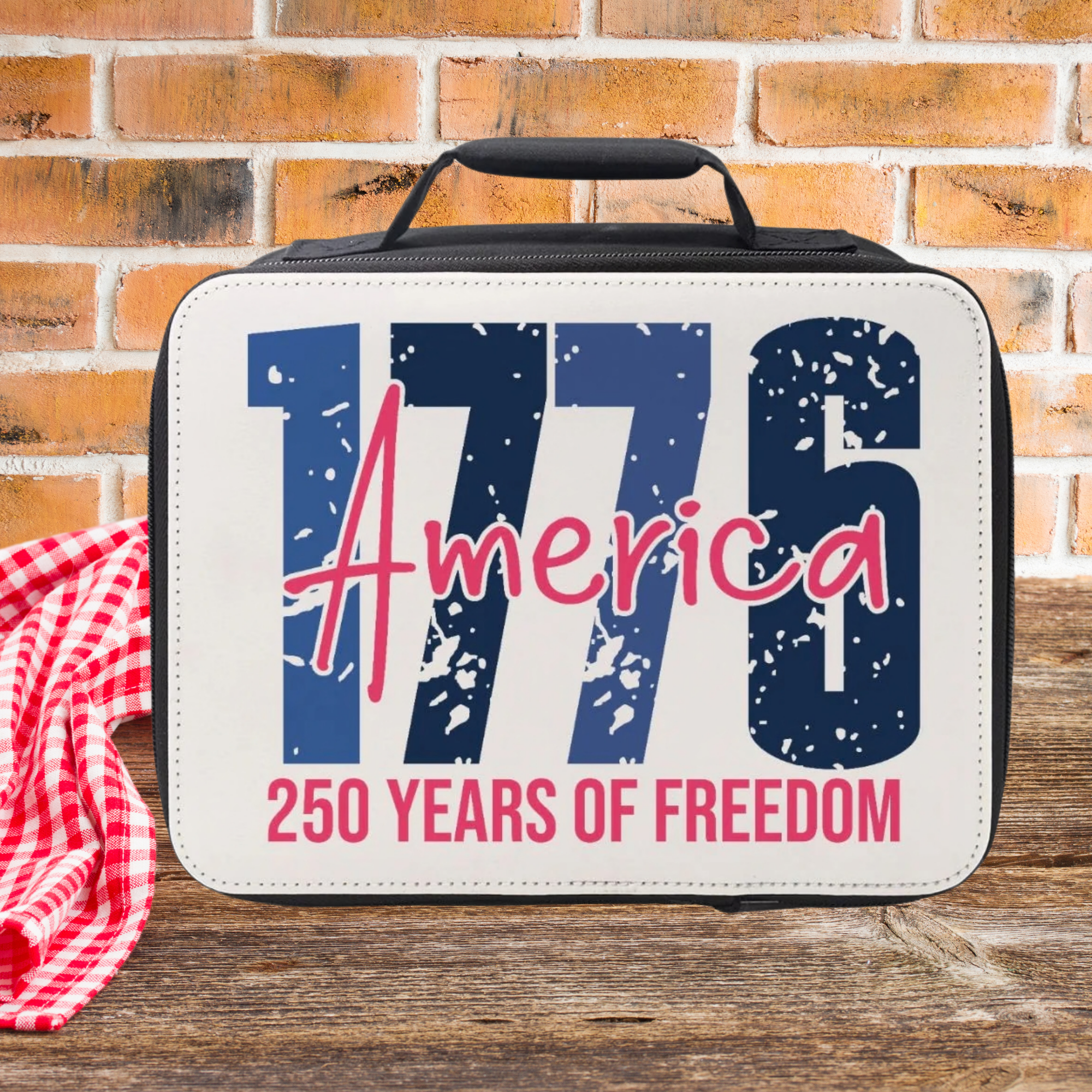Lunch bag with '1776 America 250 Years of Freedom' text on a picnic table  against a brick wall background