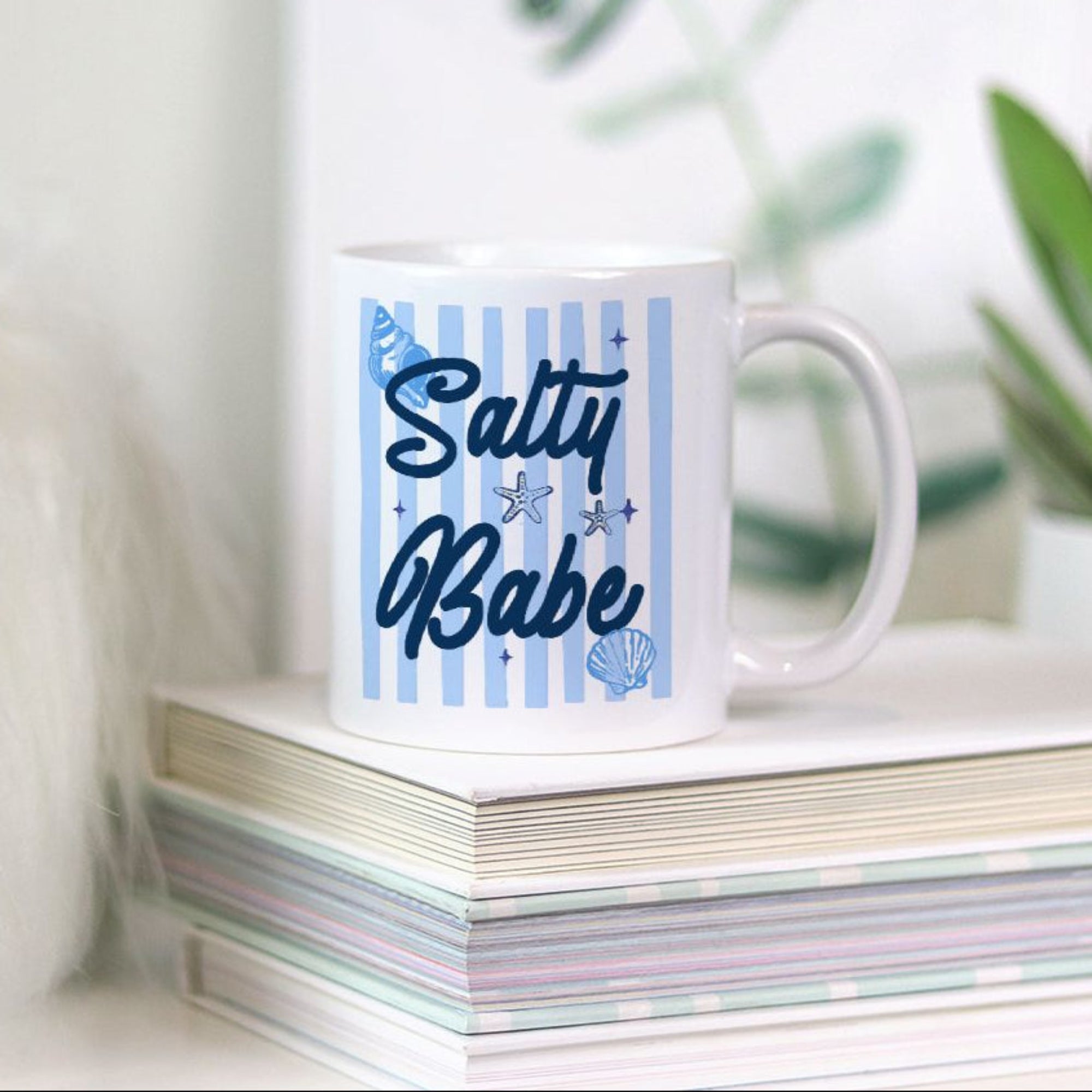 11oz. Mug with 'Salty Babe' text on a stack of books with a plant in the background