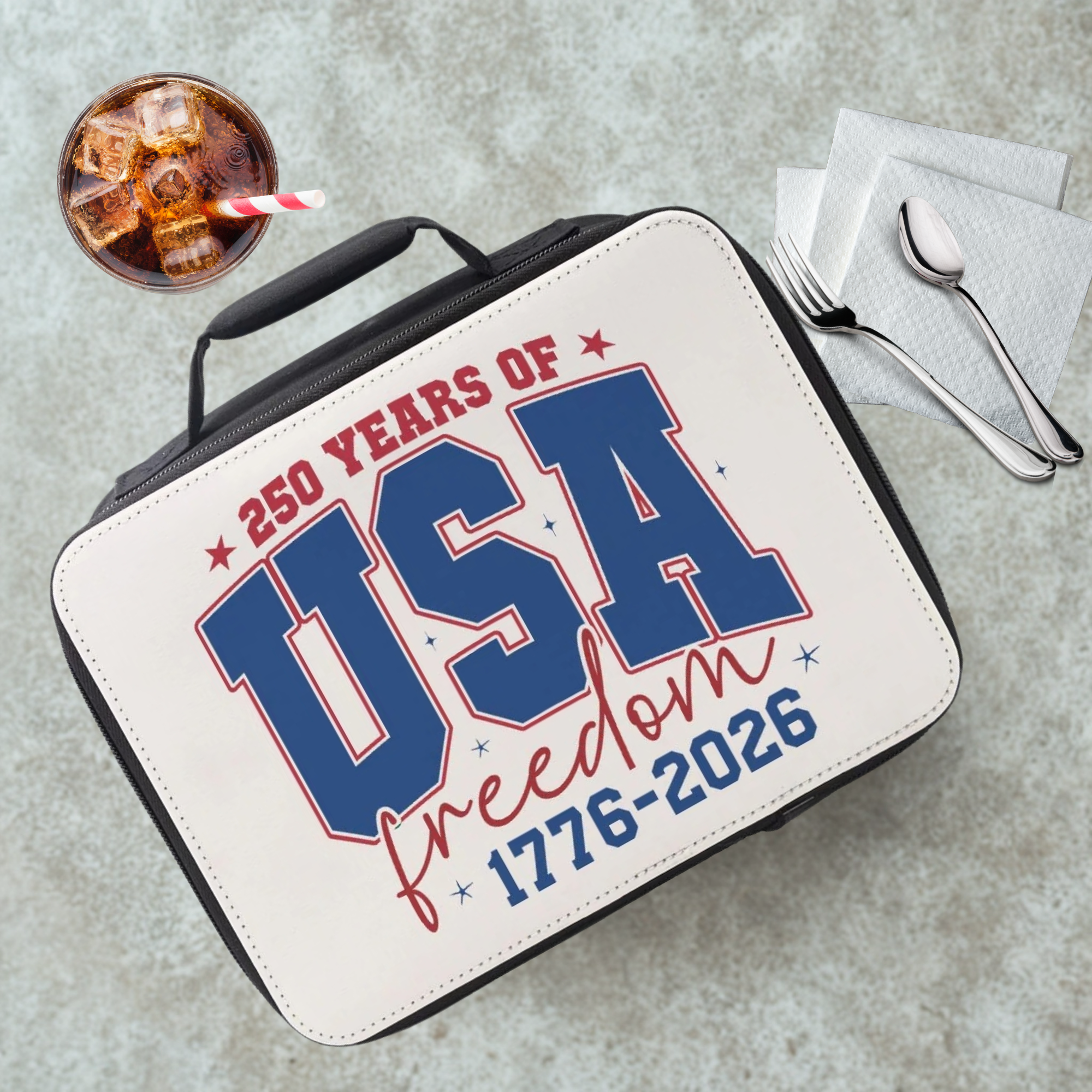  insulated lunch bag with '250 Years of USA Freedom 1776-2026' text on a cafeteria table with a drink and napkins.