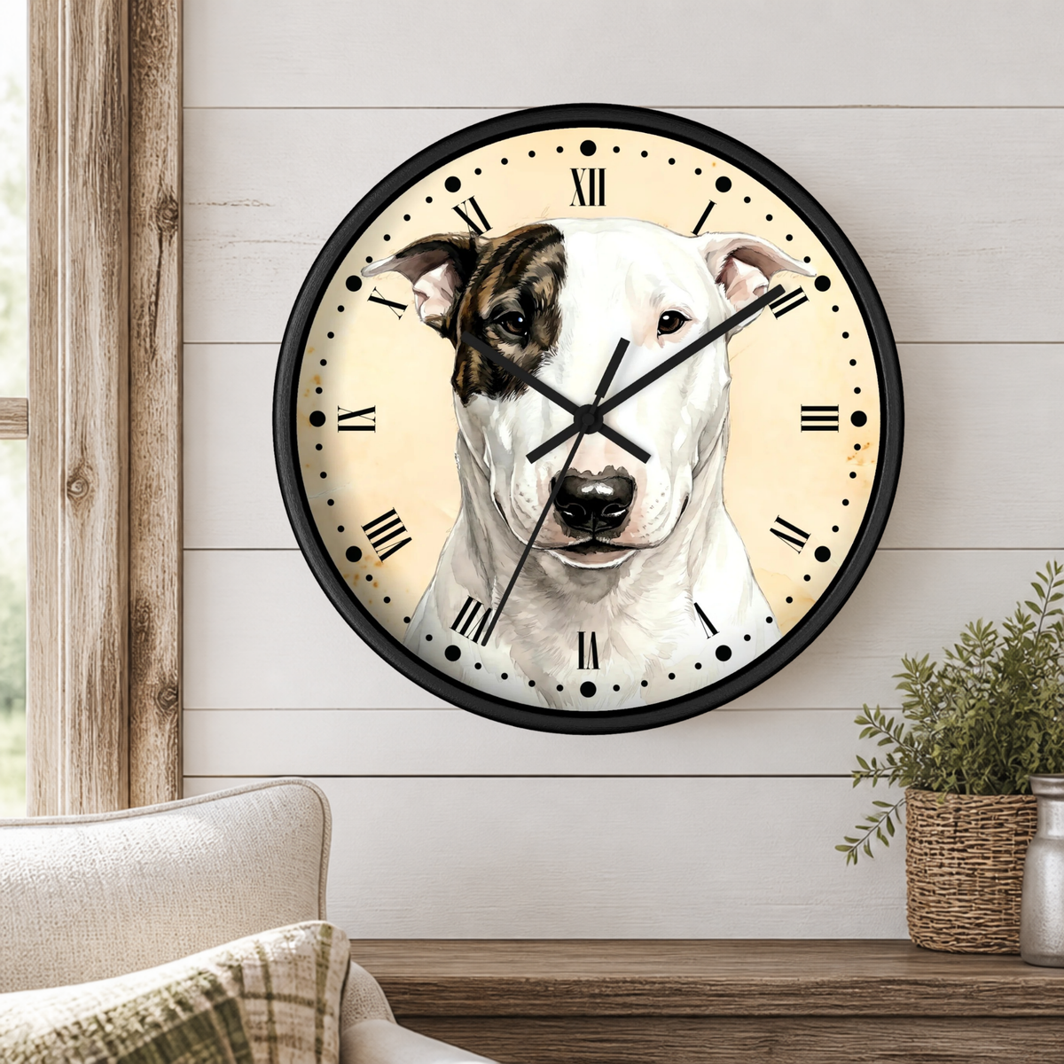 A round wall clock with a black frame and a printed dog face on the dial, mounted on a white shiplap wall above a wooden table with a plant and part of a sofa visible.