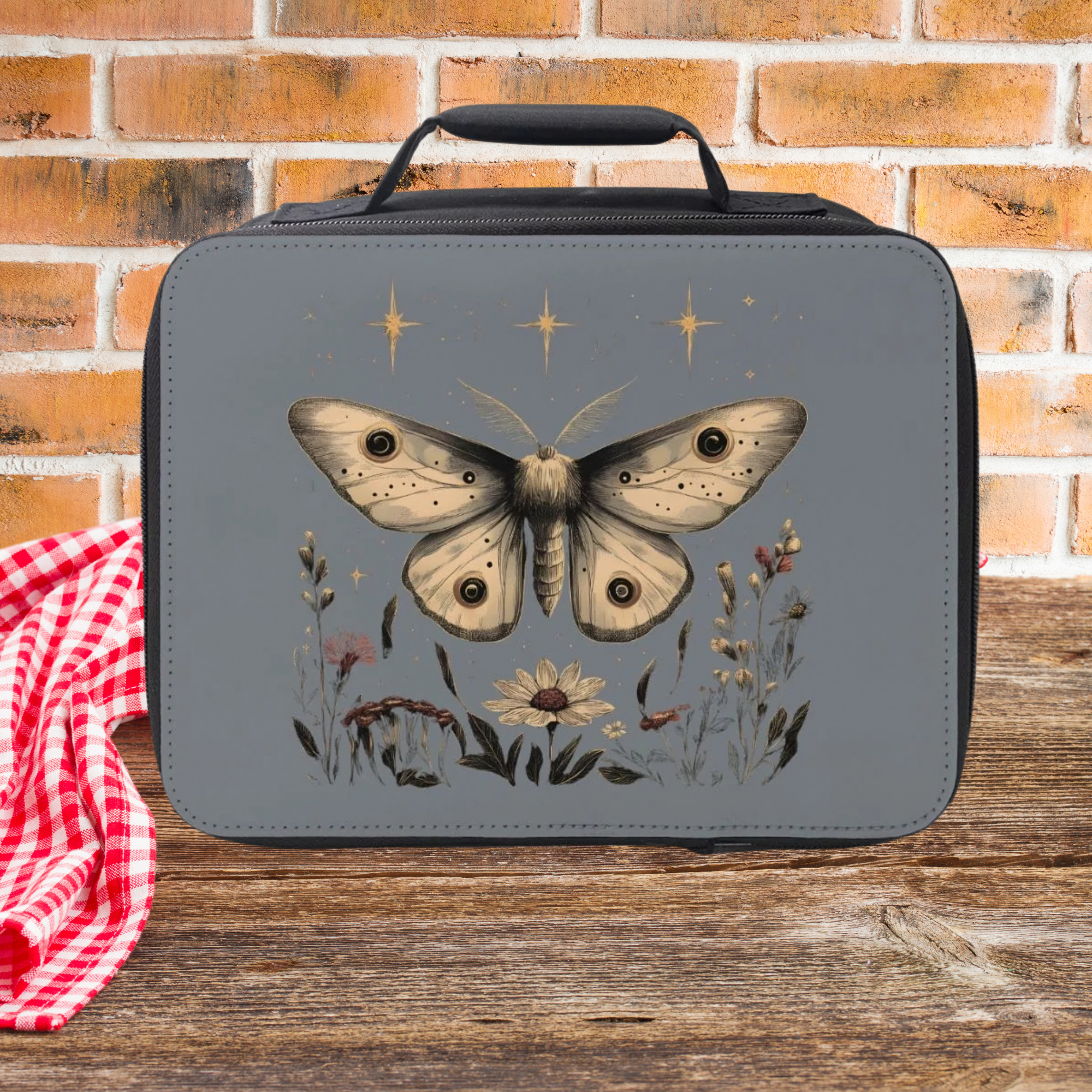 Lunch bag with a celestial moth design on a wooden picnic table and brick wall background