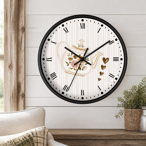 A round wall clock with a black frame and a white face featuring a floral teapot illustration, Roman numerals, and gold heart accents, mounted on a white shiplap wall above a wooden table with a plant.
