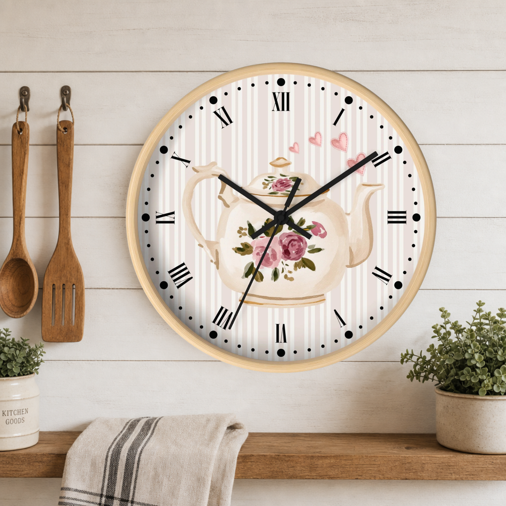 A round wall clock with a floral teapot design on the face, mounted on a white wood-paneled wall above a wooden shelf with plants and a towel. Two wooden kitchen utensils hang on the left.