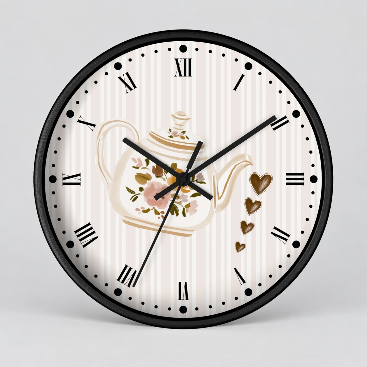 Round wall clock with a black frame, Roman numerals, and a white striped dial featuring a floral teapot illustration and gold hearts, shown on a light gray background.