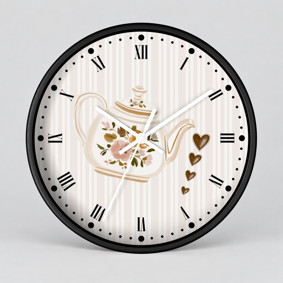 Round wall clock with a black frame, cream and white vertical stripes, black Roman numerals, and a central floral teapot illustration with gold accents and small brown hearts, shown on a light gray background.