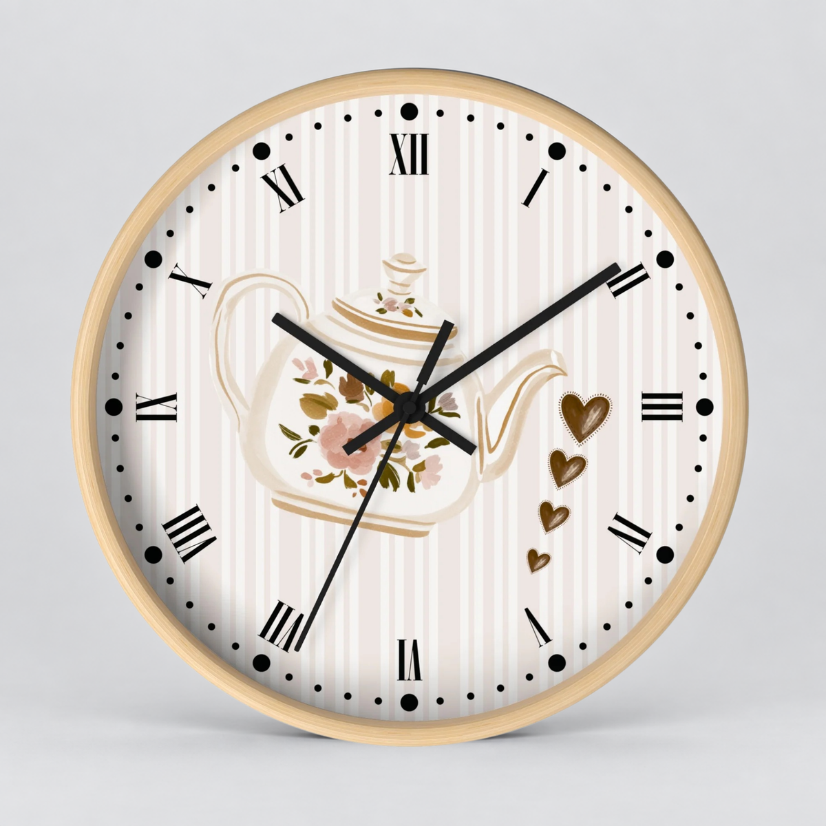 Round wall clock with a light wood frame, featuring a cream and white striped dial, black Roman numerals, black hands, and a central floral teapot illustration with decorative hearts.