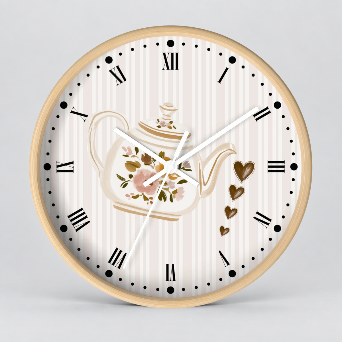 Round wall clock with a light wood frame, featuring a cream and white striped dial, black Roman numerals, a floral teapot illustration, and gold heart accents on a light gray background.