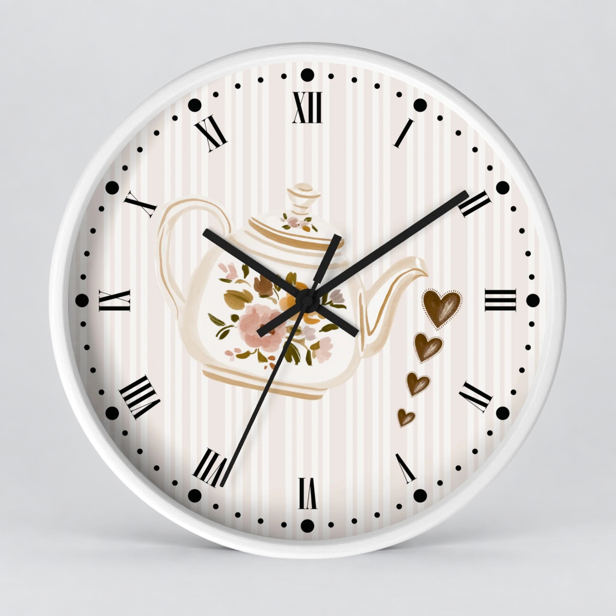 A round wall clock with a white frame and a decorative face featuring vertical cream stripes, black Roman numerals, black hour and minute hands, a floral teapot illustration, and small gold hearts on a light gray background.