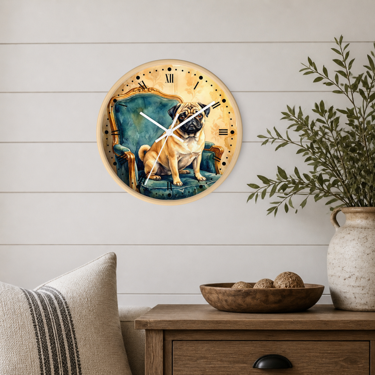 A round wall clock with a light wood frame hangs on a white shiplap wall above a wooden side table. The clock face features a painted pug dog sitting on a blue chair against a warm gold background.