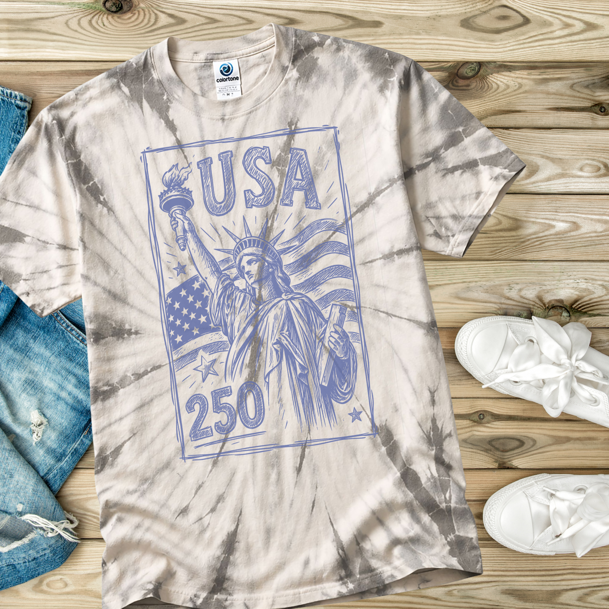 Tie-dye t-shirt with 'USA 250' graphic on a wooden surface with jeans and sneakers.