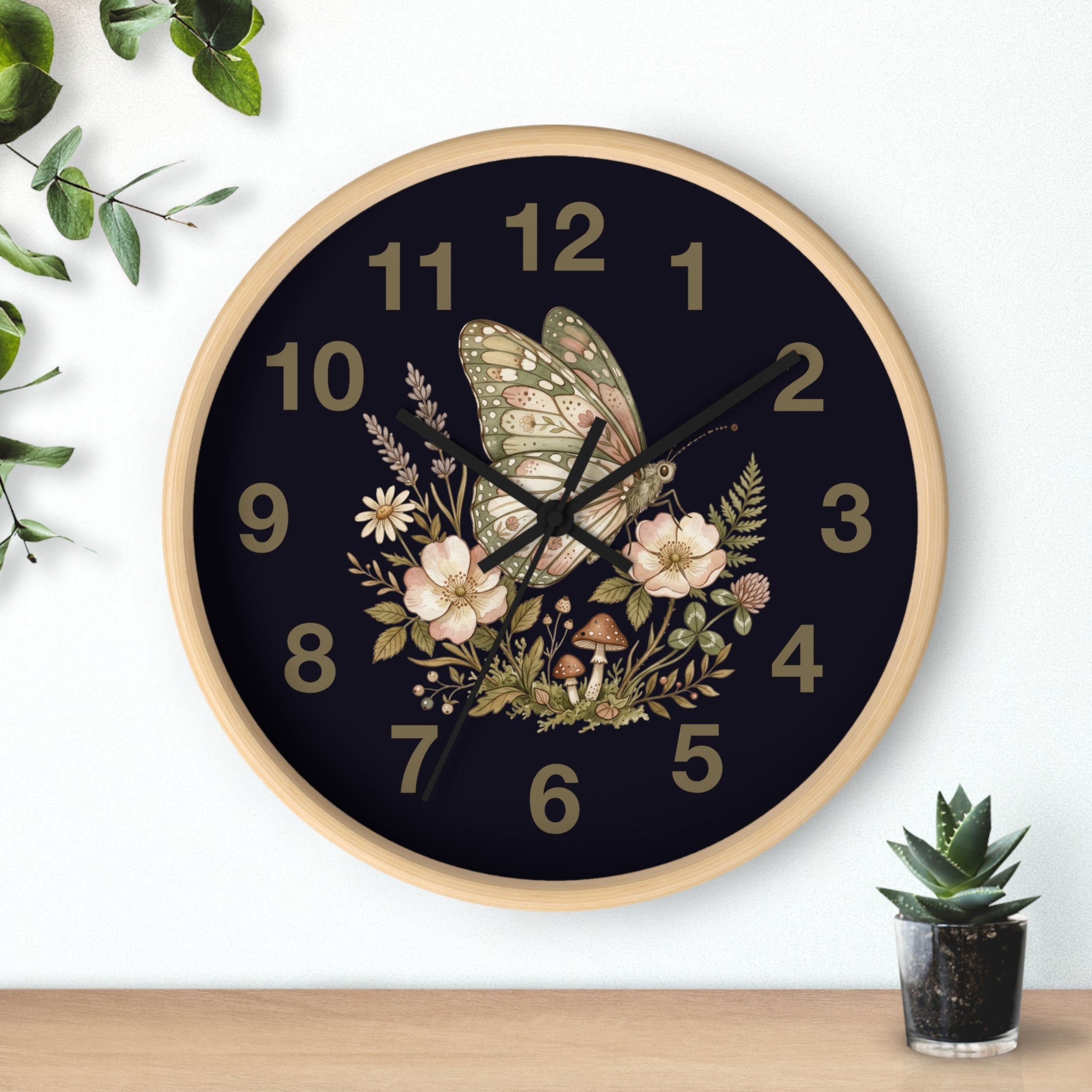 Decorative natural wood wall clock with butterfly and floral design on a black background, placed on a white wall with a plant and small pot in the foreground.