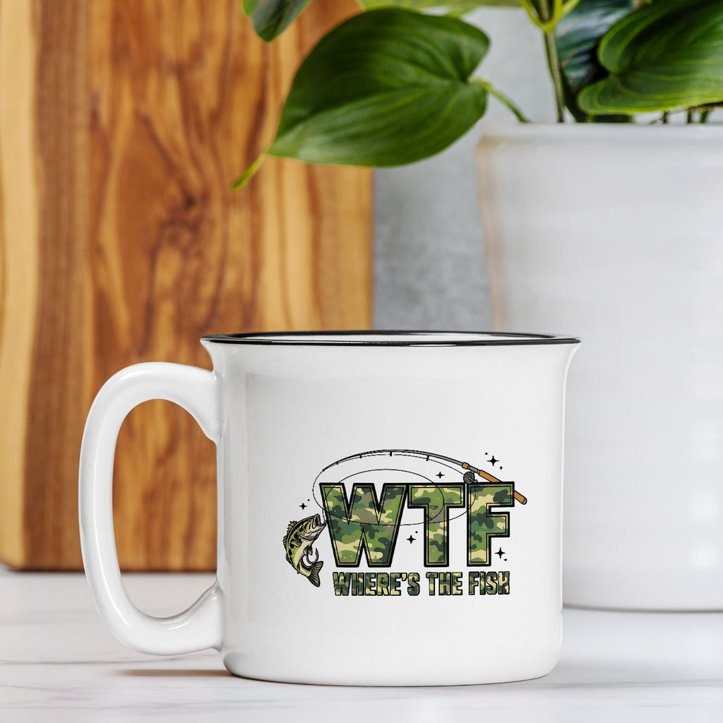 White mug with 'WTF Where's the Fish' design on a wooden surface with a plant in the background